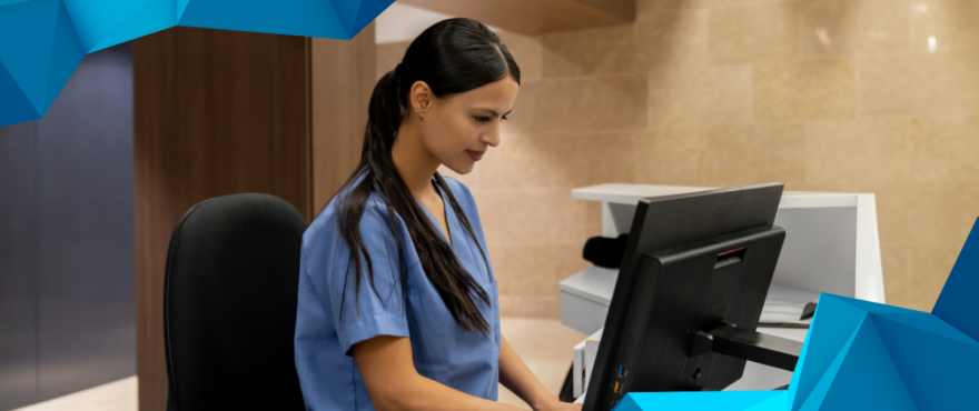 A female healthcare professional wearing blue scrubs is seated at a reception desk, focused on a computer screen. The setting is a modern medical facility with a sleek, well-lit interior. The image is framed with geometric blue design elements.